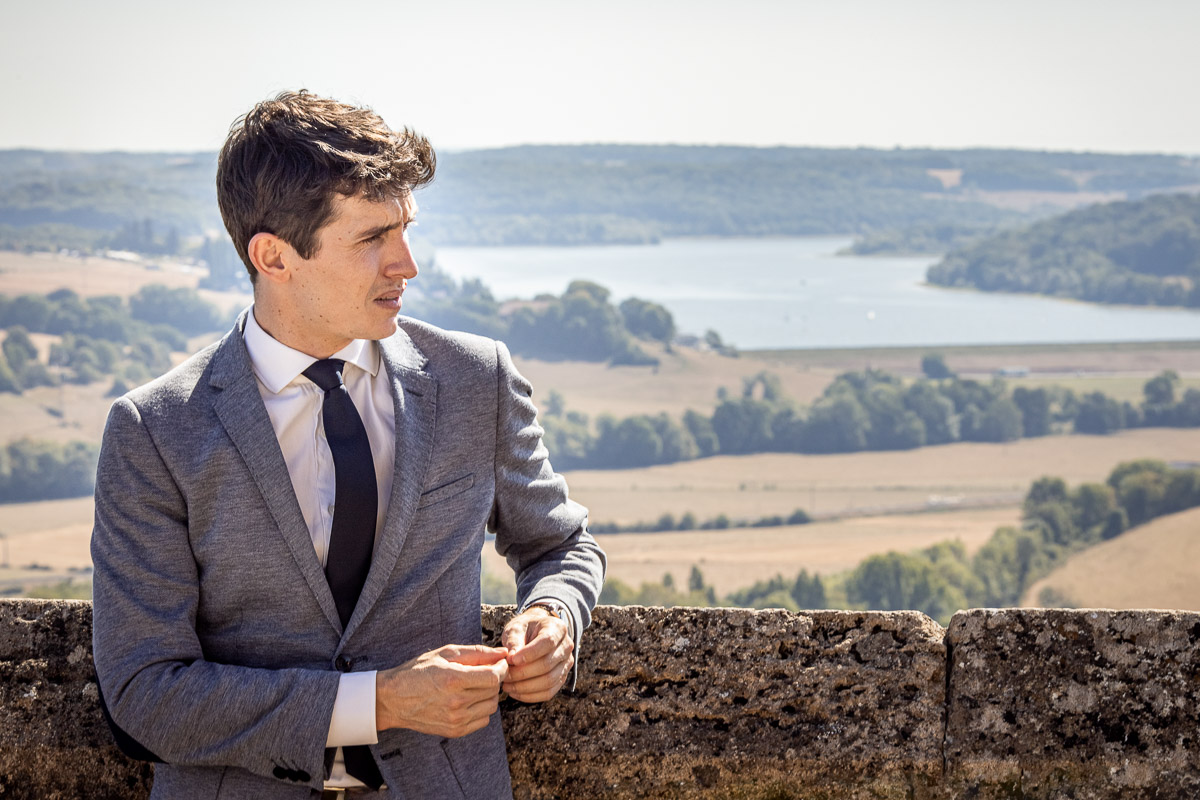 Un homme en costume debout sur un mur de pierre pour une séance photo de mariage par un photographe à Langres.