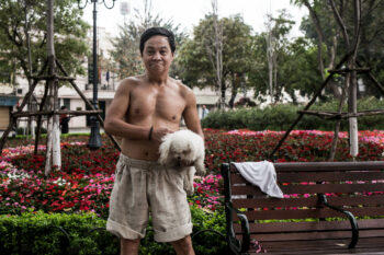 A man walking a dog in a park in Vietnam.