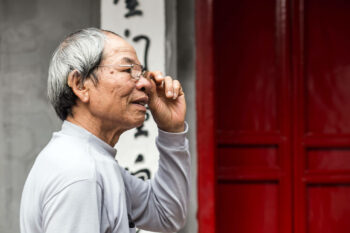 An Asian man talking on the phone in front of a red door in Vietnam.