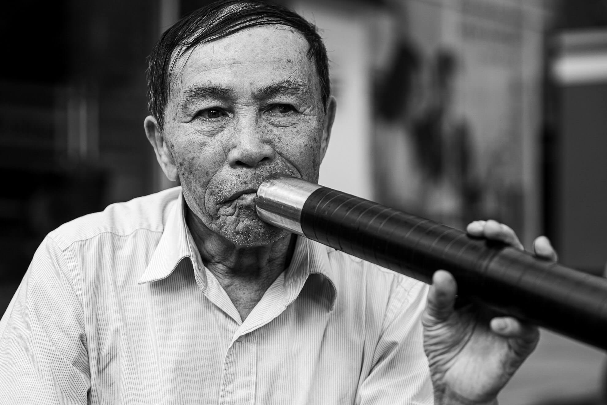 A black and white photo of an old man smoking a pipe in Vietnam.