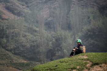 Ein Mann sitzt mit einem Korb auf dem Rücken auf einem Hügel in Vietnam.