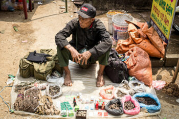 Ein Mann sitzt in Vietnam mit vielen Gegenständen auf dem Boden.