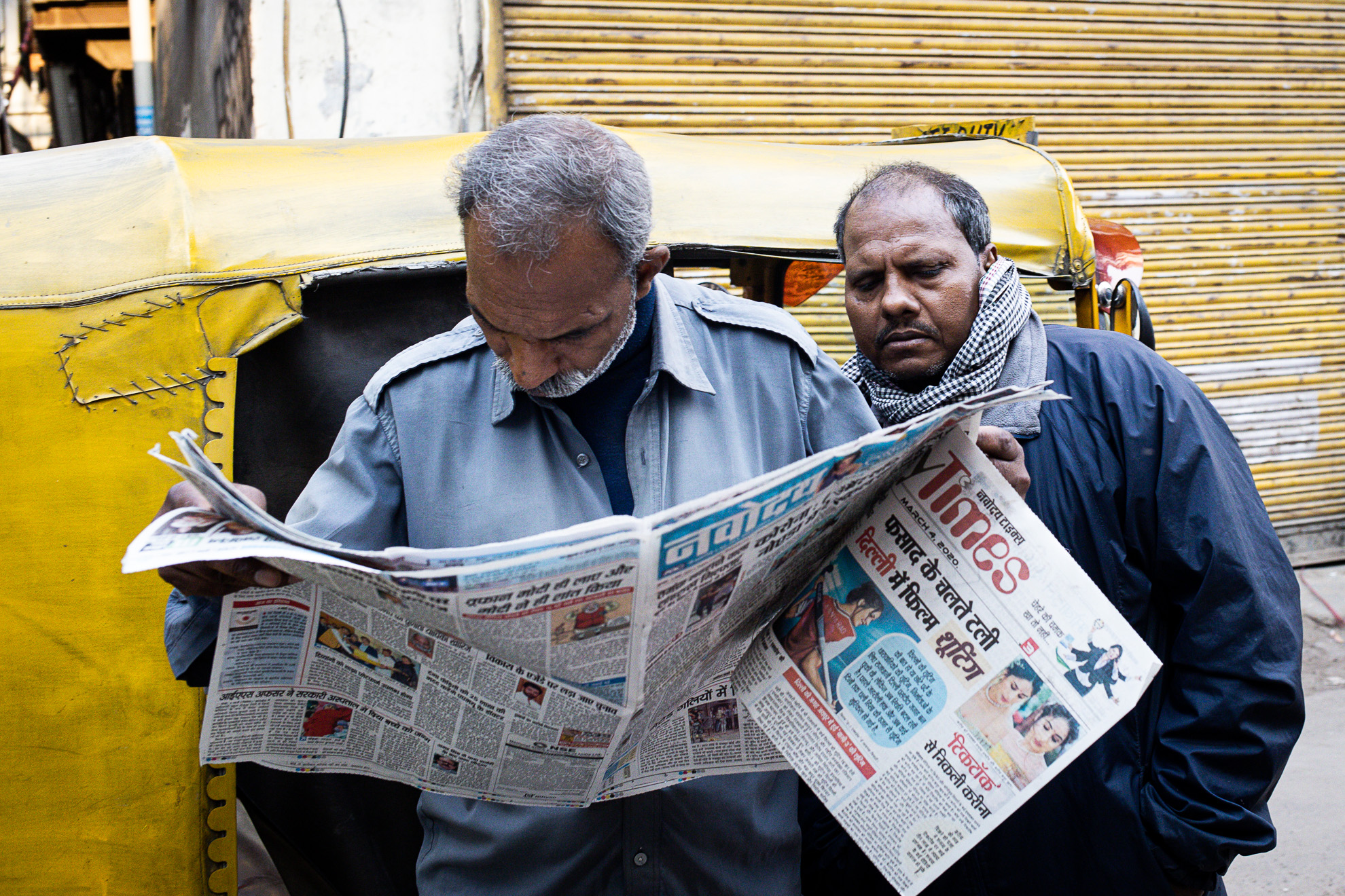 Deux hommes lisant un journal devant un tuk tuk jaune en Inde.