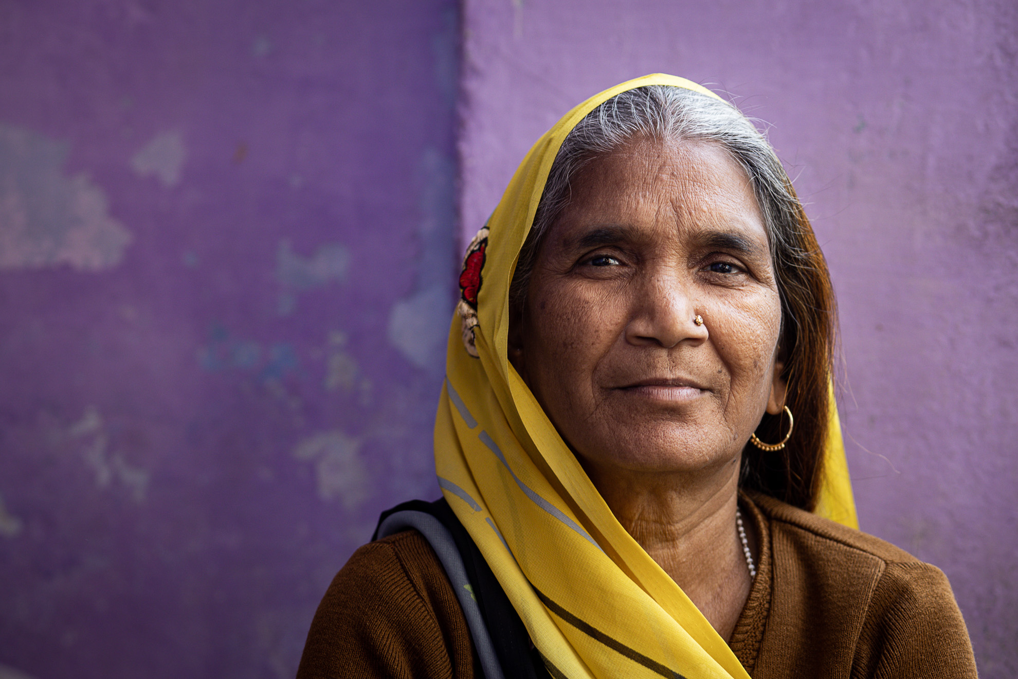 Une Indienne portant un foulard jaune devant un mur violet en Inde.