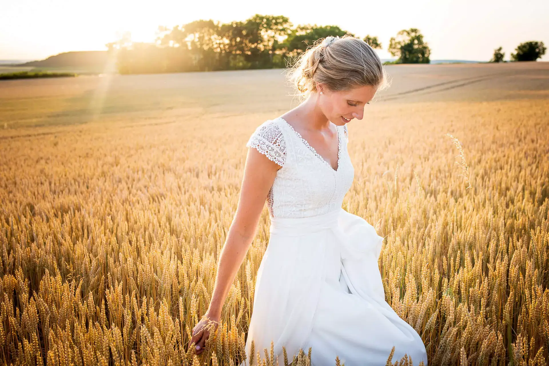 Une jeune marié au milieu d'un champ au couché du soleil.