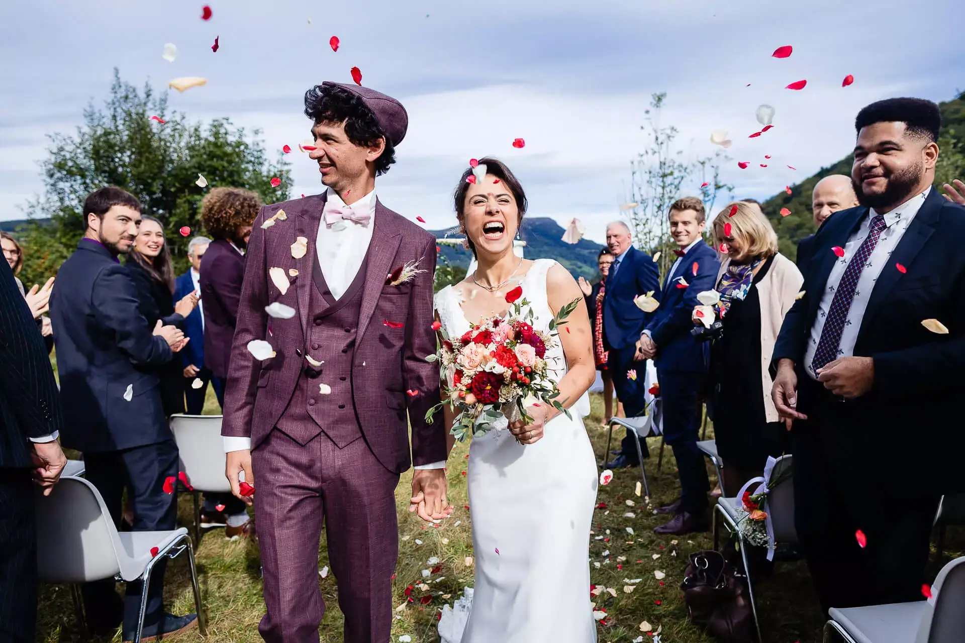 La mariée avec son bouquet de fleurs, aux coté de son mari, au milieu des pétales lancés par les invités.