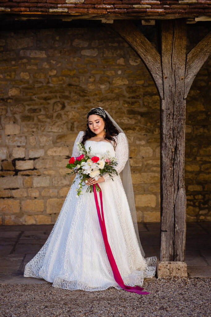 Une mariée en robe de mariée pose devant une vieille grange.