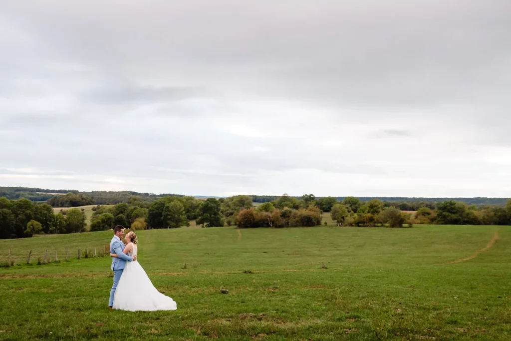 Une mariée et un marié debout dans un champ avec un ciel nuageux.