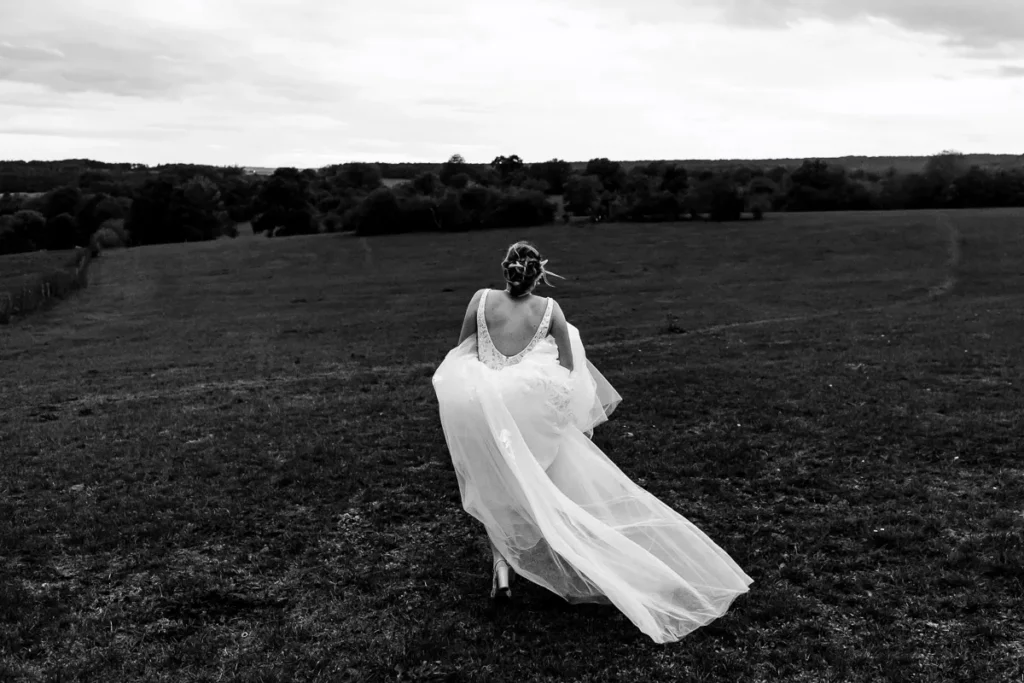 Photo en noir et blanc d'une mariée courant dans un champ.