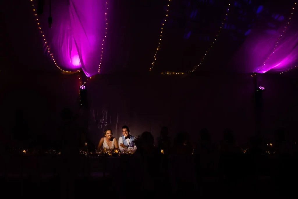 Une mariée et un marié assis à une table sous des lumières violettes.