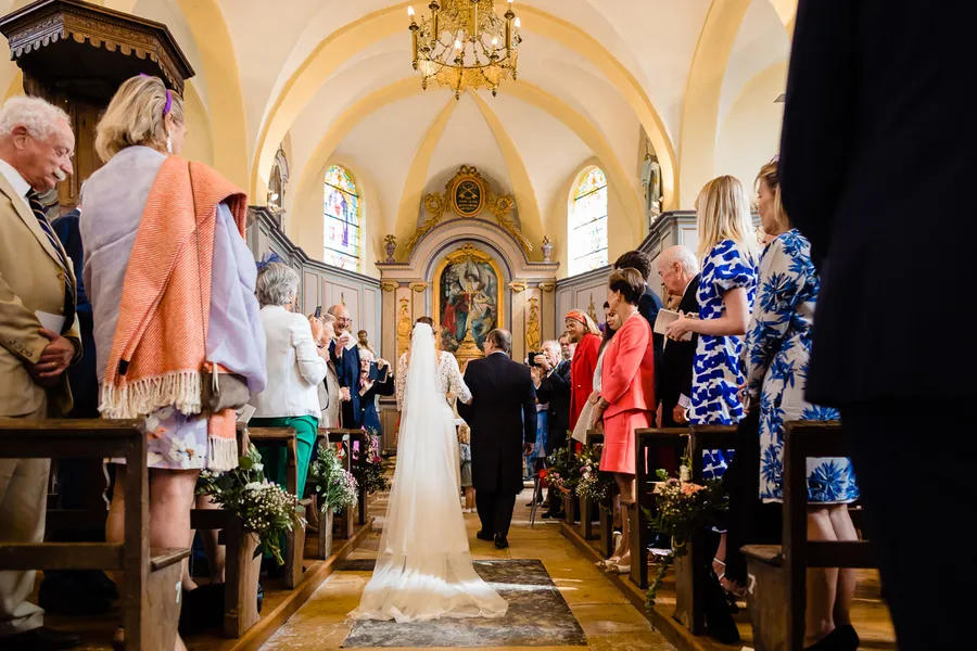 Une mariée marche dans l’allée d’une église.