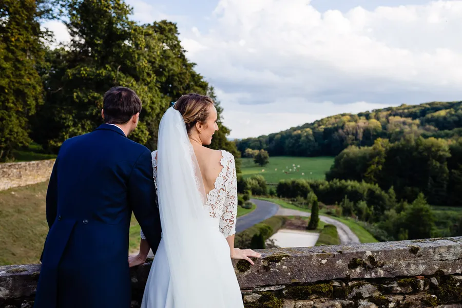 Une mariée et un marié debout sur un mur donnant sur un champ.