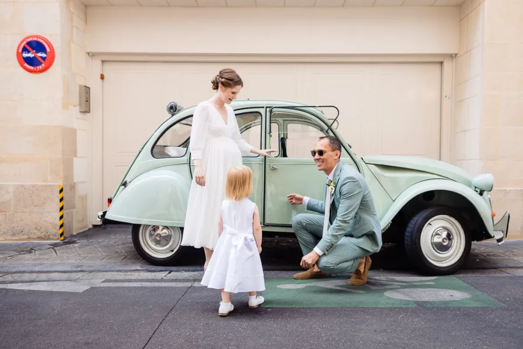 Une mariée et un marié debout à côté d’une voiture verte.