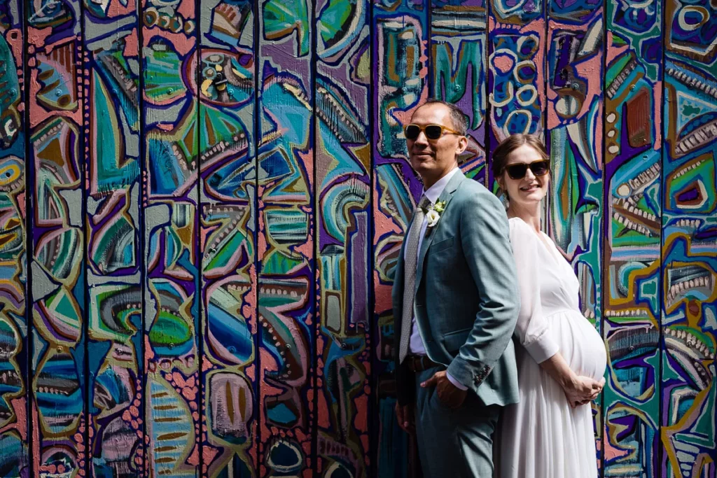 Un couple enceinte debout devant un mur coloré.