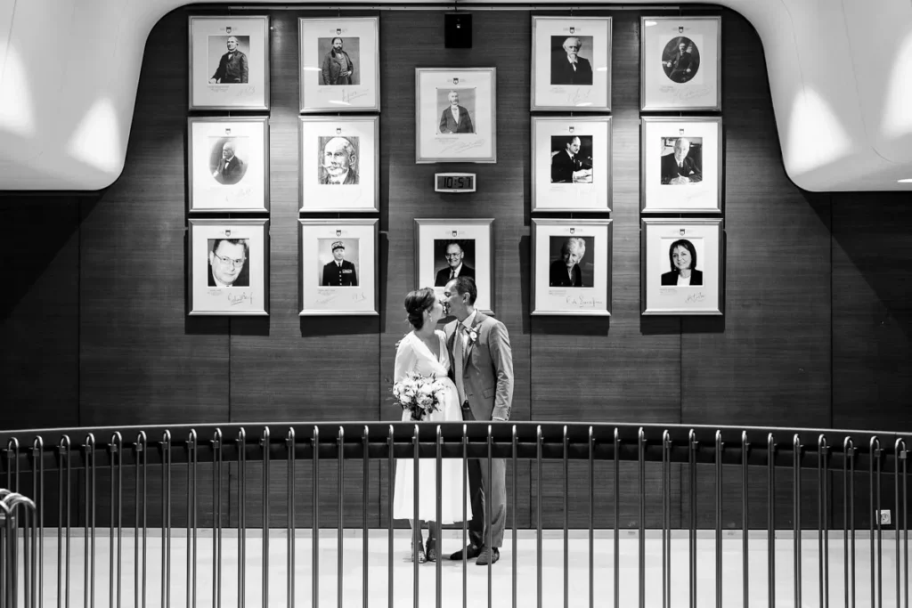 Des mariés debout devant un mur de photos.