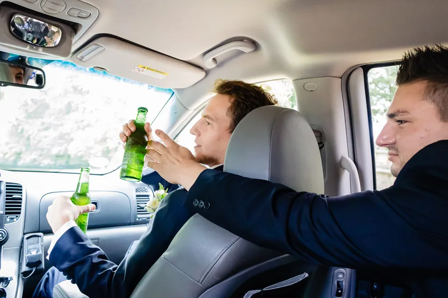 Deux hommes boivent de la bière sur la banquette arrière d’une voiture.