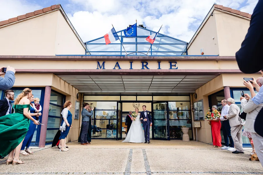 Une mariée et un marié debout devant un bâtiment avec des drapeaux.