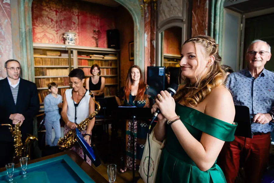 Une femme vêtue d’une robe verte tient un microphone devant un groupe de personnes.