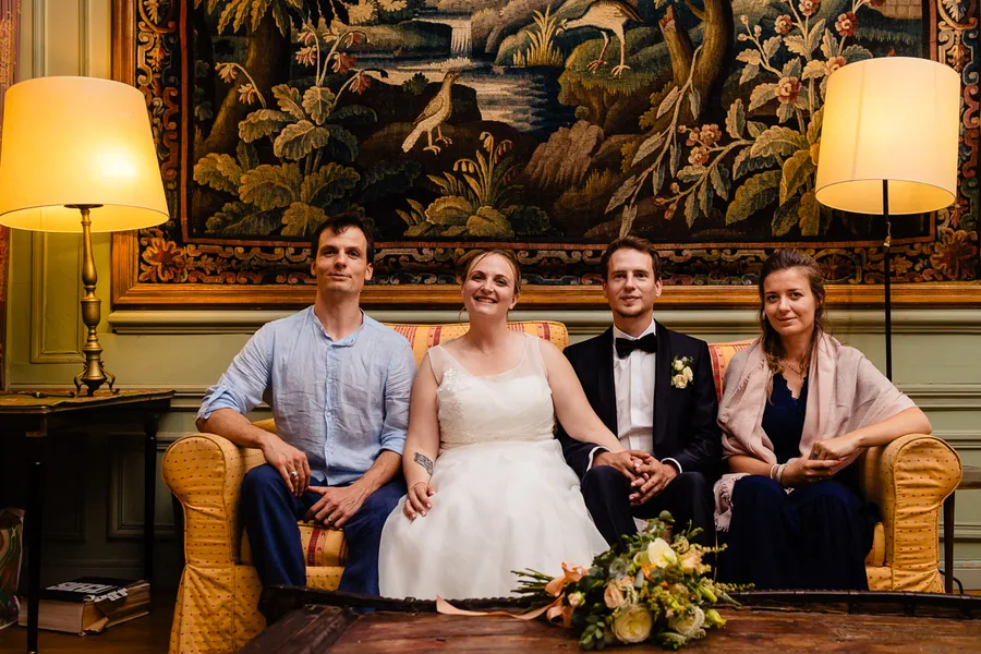 Une fête de mariage est assise sur un canapé devant une tapisserie.