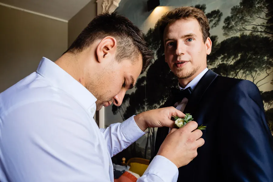 Un homme en smoking aide un autre homme avec sa boutonnière.