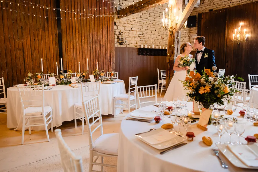 Une mariée et un marié debout devant une table dans une grange rustique.