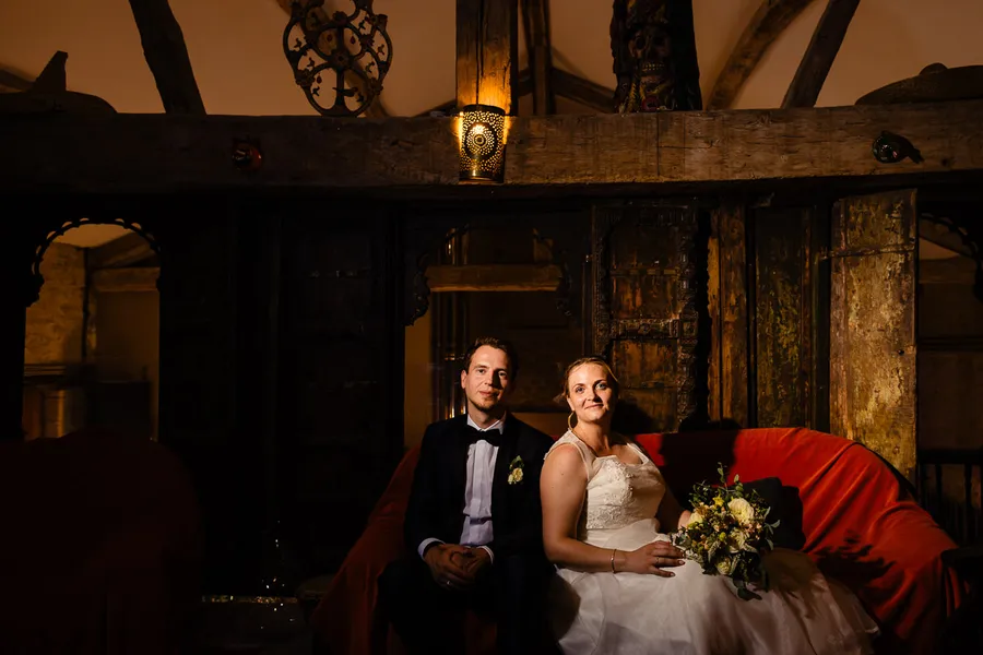 Une mariée et un marié assis sur un canapé rouge dans une pièce sombre.